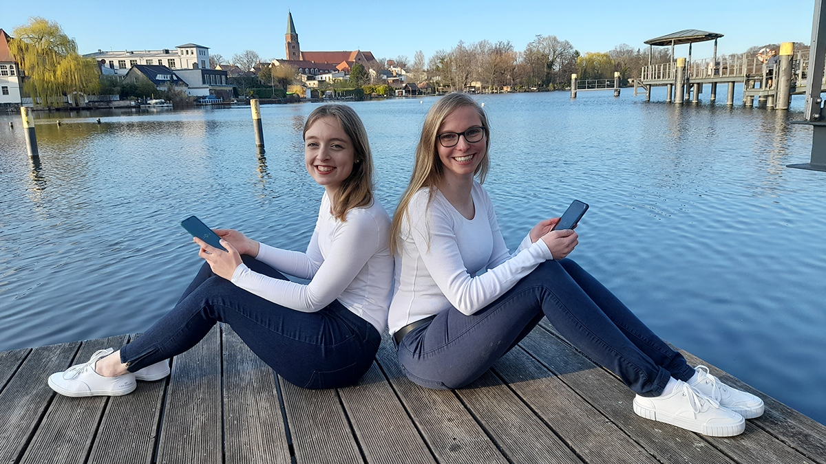  LAOLA-Gründerinnen Laura Dietrich und Annika Keller sitzend auf einem Steg am See