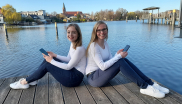 LAOLA-Gründerinnen Laura Dietrich und Annika Keller sitzend auf einem Steg am See